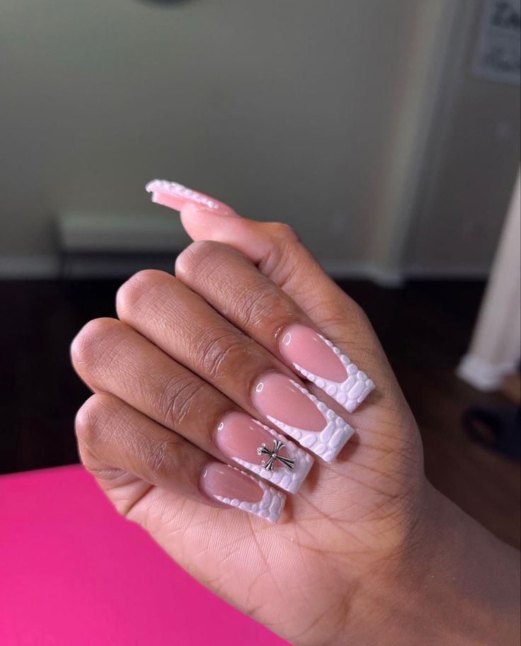 Sophisticated Nail Design: Long Acrylic Tips with Nude Base, Textured White Tips, and Metallic Charm Accent.