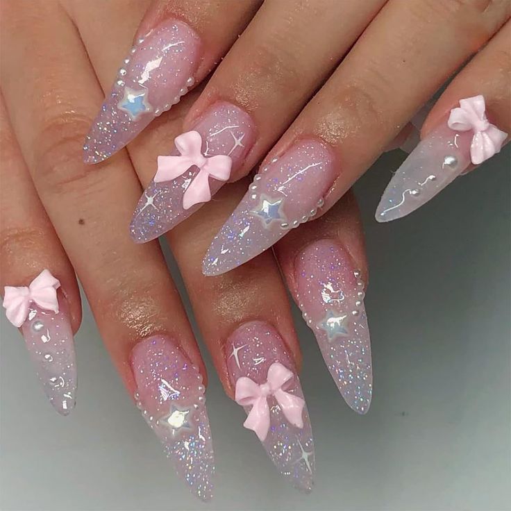 Playful Glistening Ombre Nail Design: Pale Pink to Translucent White with Bows and Rhinestones.