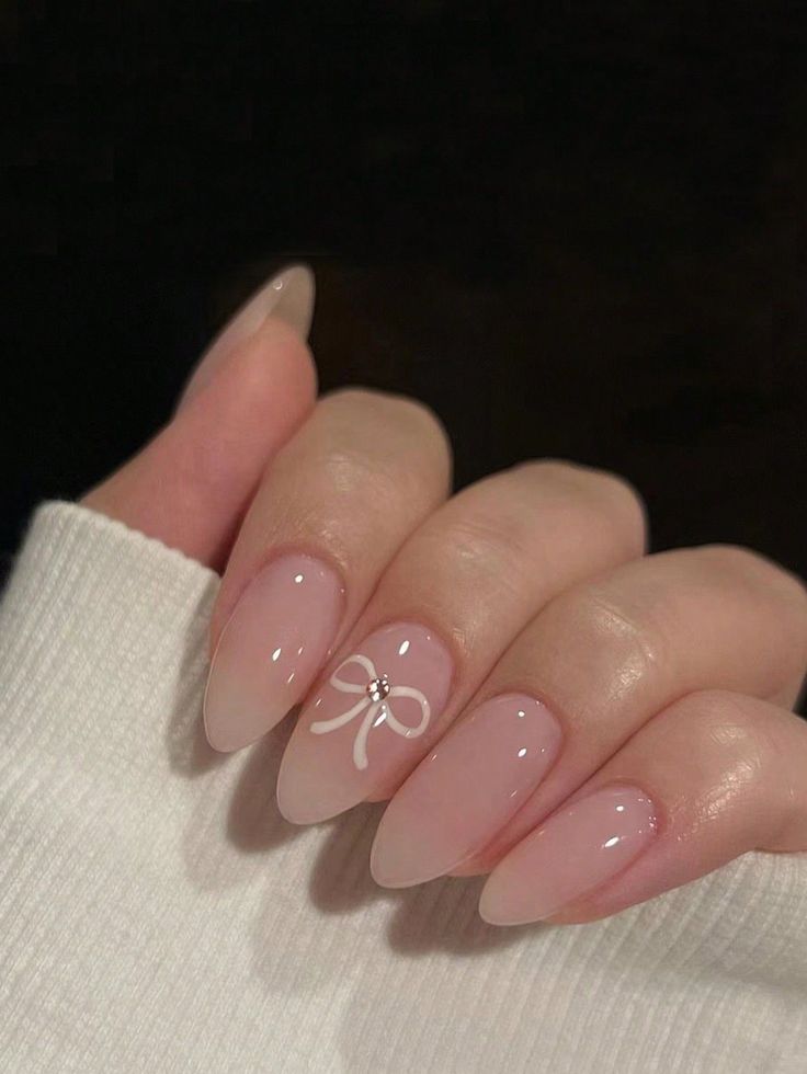 Chic Elegant Nail Design: Soft Nude Base with Glossy Finish, White Bow Detail, and Sparkling Gemstone.