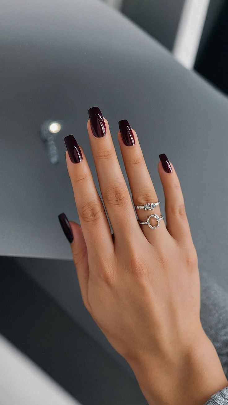 Chic Dark Burgundy Nails with Glossy Finish and Glam Silver Rings.