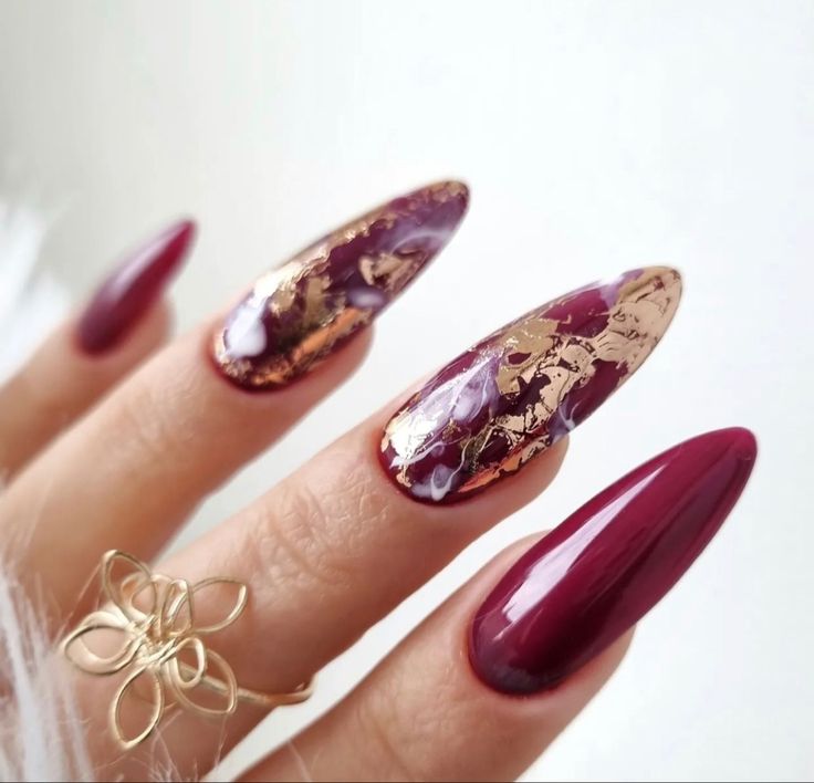 Sophisticated Burgundy Almond Nails with Gold Leaf Accents and Glossy-Marbled Textures.