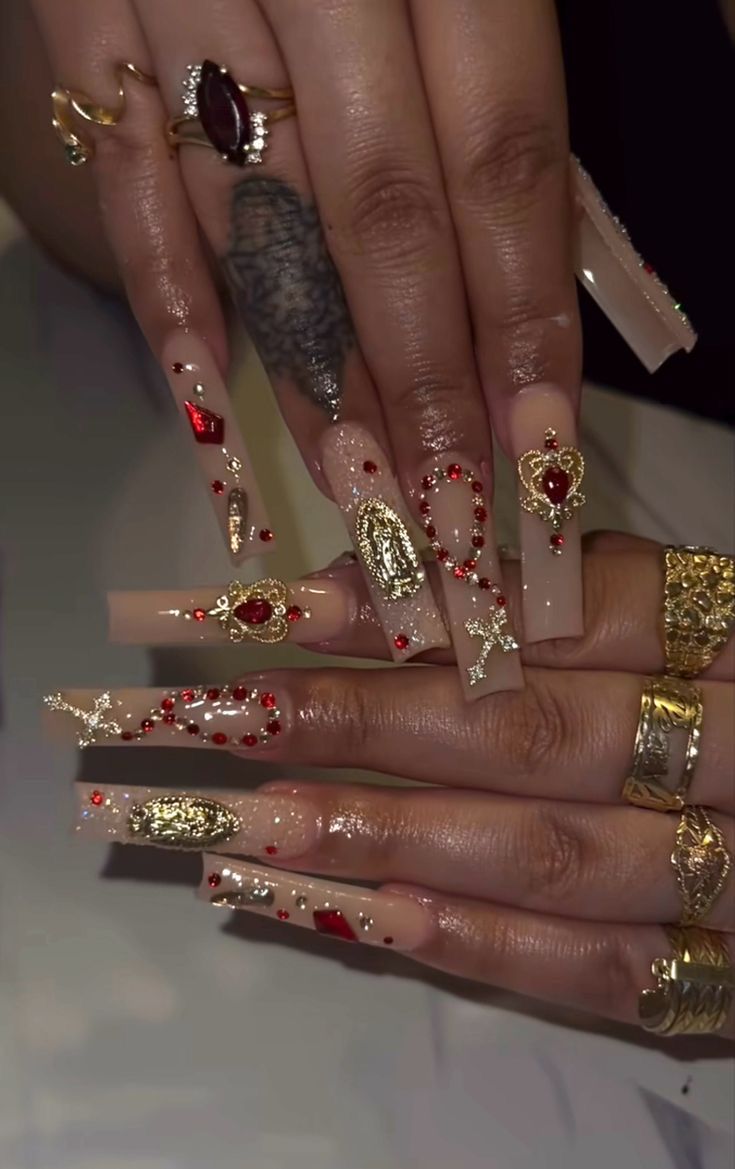 Elegant Nude and Gold Nail Design with Intricate Red Gems and Charms.