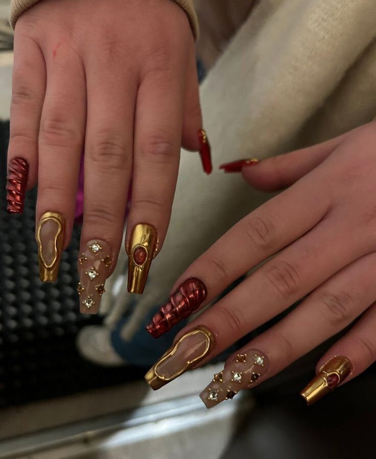 Striking Nail Art: Bold Red and Gold Designs with Textures and Gemstone Accents.