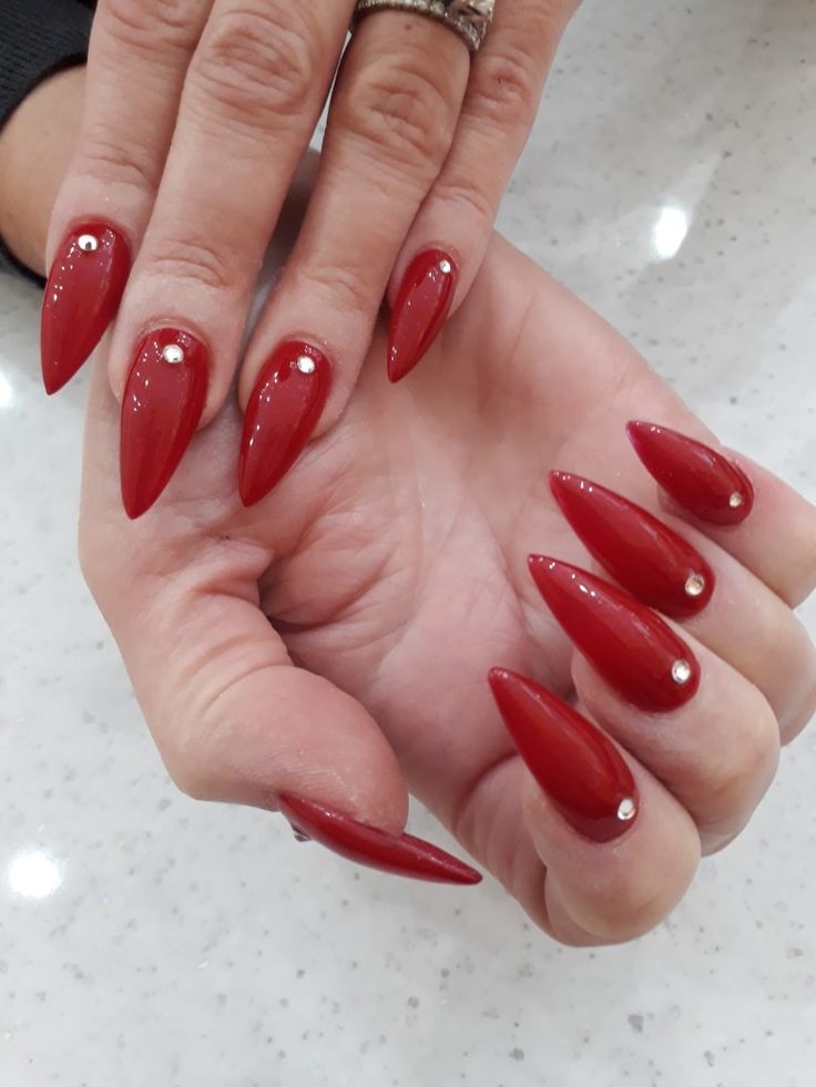 Elegant Red Almond Nails with Glossy Finish and Sparkling Silver Embellishments.