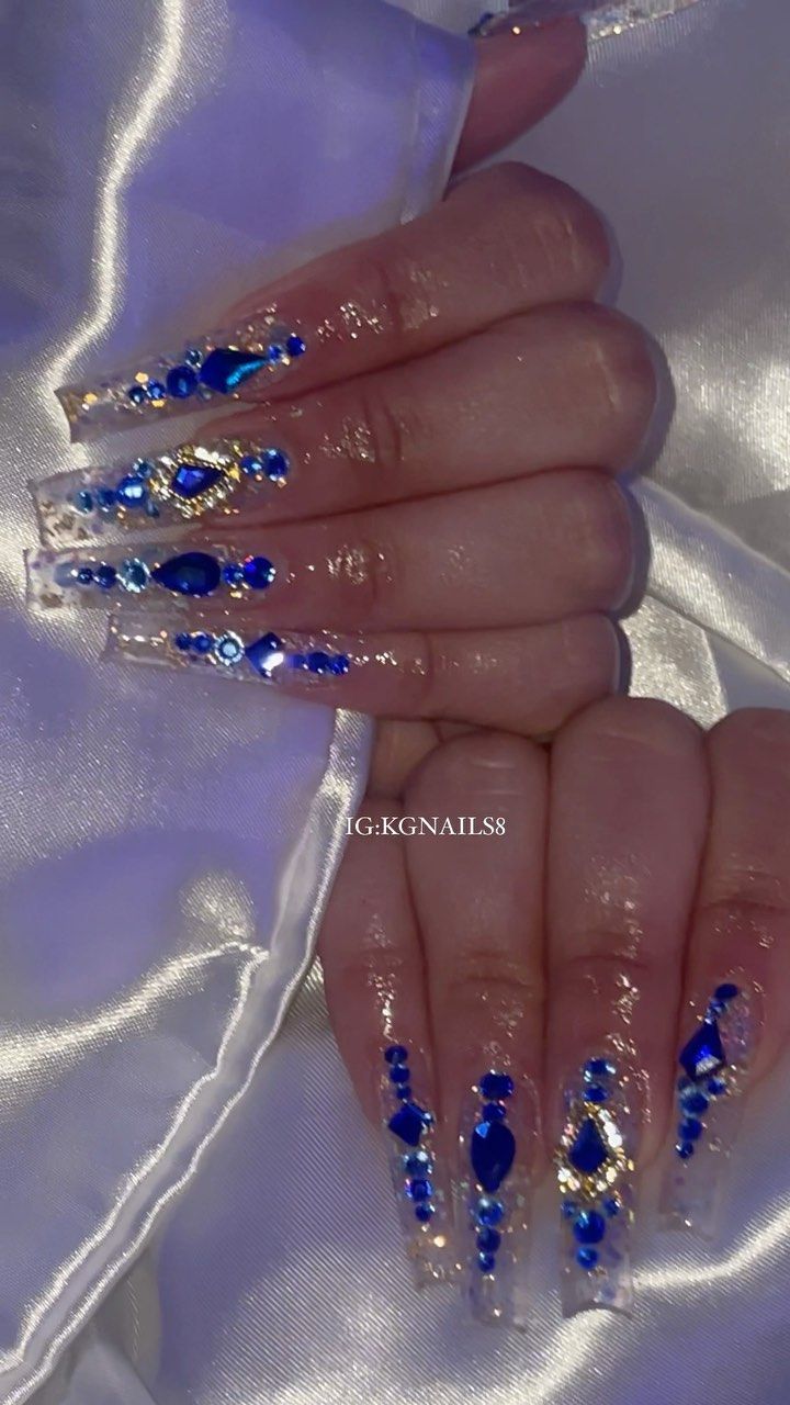 Sophisticated Elegant Nail Design with Clear Base, Blue and Gold Embellishments, and Intricate Gem Patterns.