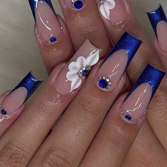 Chic Nail Design: Glossy Blue Tips with Floral Details and Gemstone Accents.