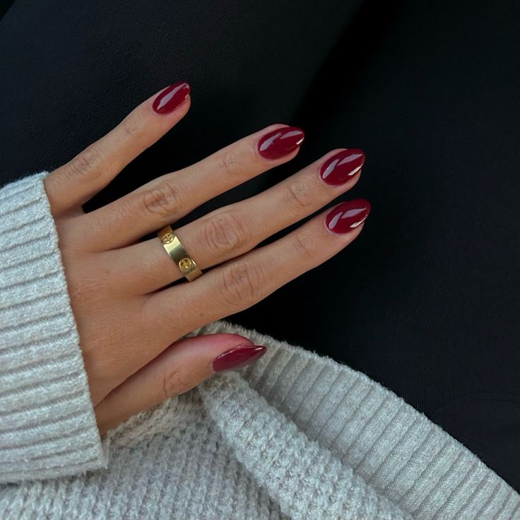 Sophisticated Burgundy Almond Nails with Glossy Finish and Gold Ring: A Chic and Cozy Look.