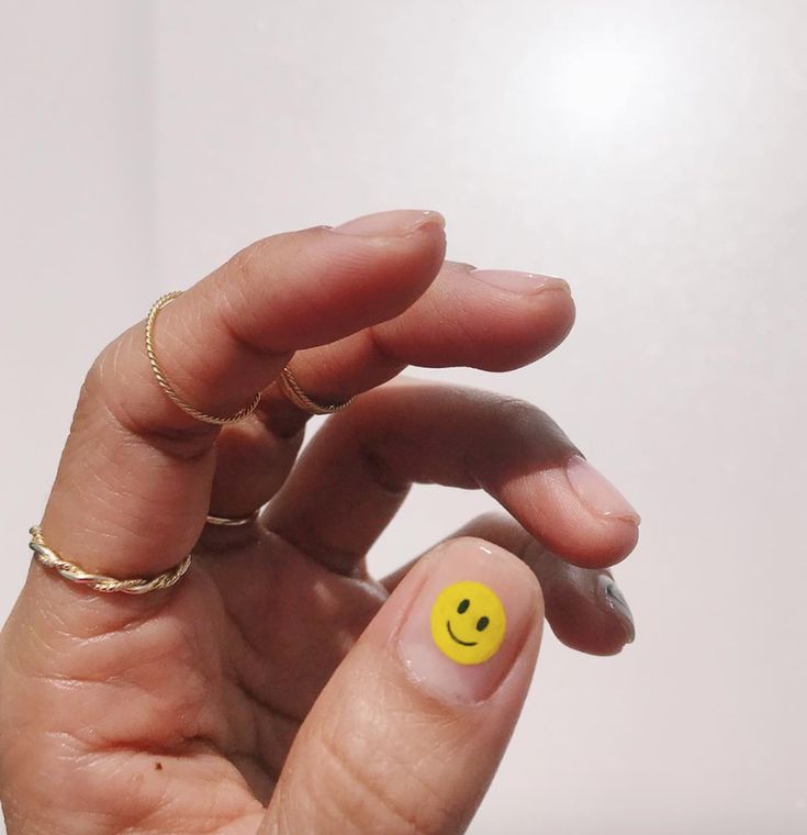 Playful Yellow Smiley Nail Design Enhanced by Delicate Rings for a Cheerful Manicure.