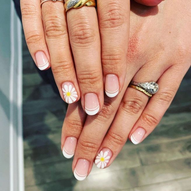 Chic French Tip Manicure with Playful Daisy Accents and Elegant Rings.