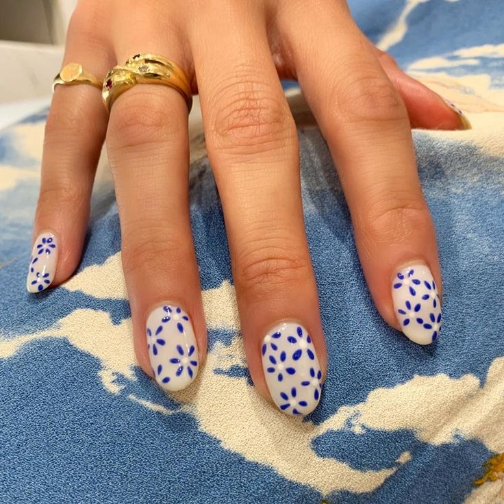 Charming Floral Nail Art: Soft White Base with Intricate Blue Flowers and Stylish Rings.