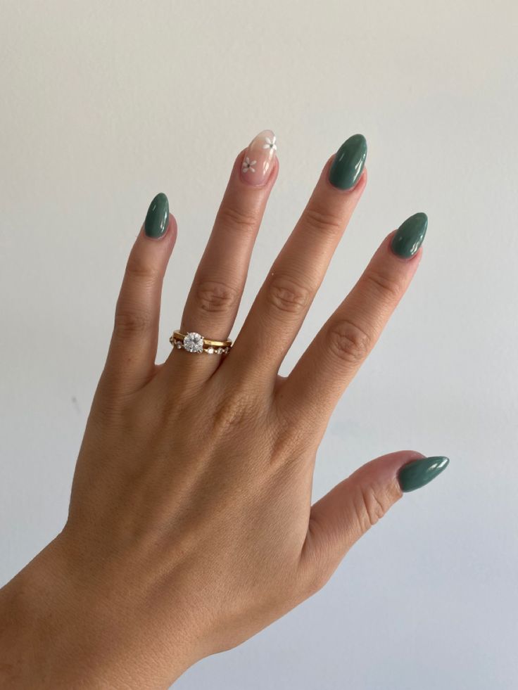 Elegant Deep Green and Nude Nail Design with Floral Accent and Gold Rings.