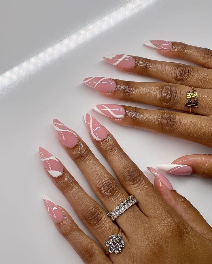 Chic Almond-Shaped Pink Nails with Elegant White Swirls and Glamorous Rings.