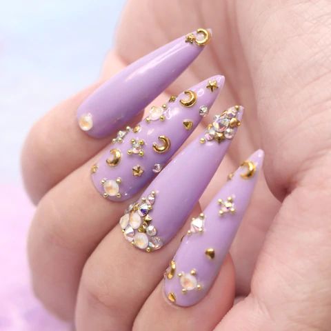 Whimsical Lavender Stiletto Nails Adorned with Sparkling Rhinestones and Celestial Embellishments.