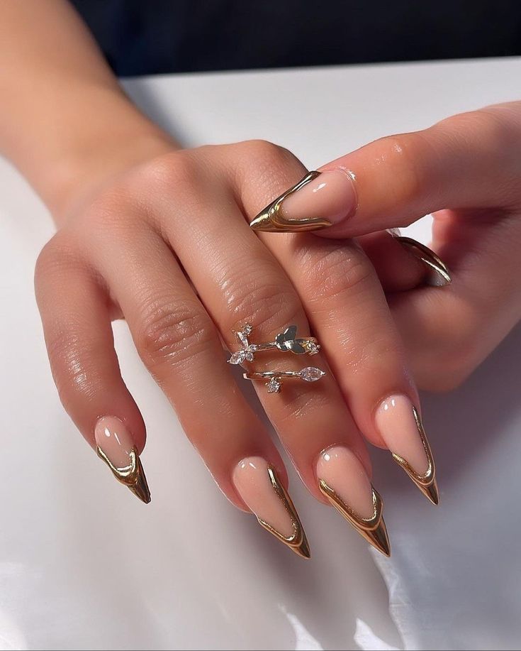 Chic Long Pointed Nail Design with Gold Accents and Nude Base.