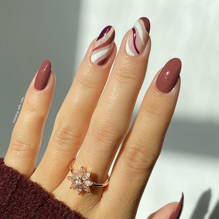 Sophisticated Maroon and Neutral Nail Design with Artistic Swirls and Glamorous Accents.