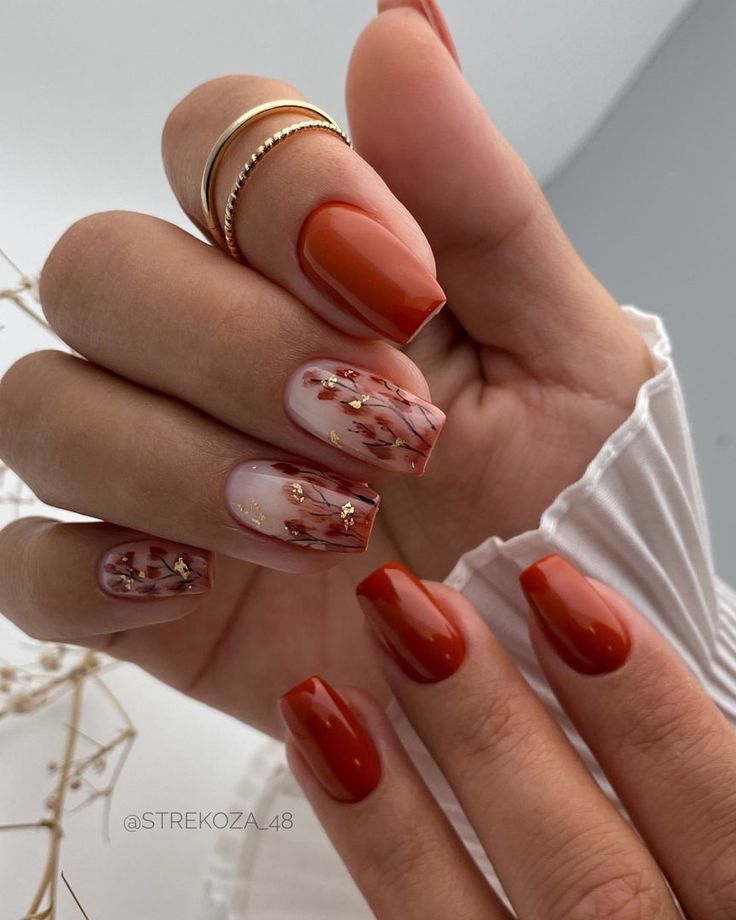 Elegant Nail Design: Warm Orange Hues with Floral Accents and Gold Embellishments.