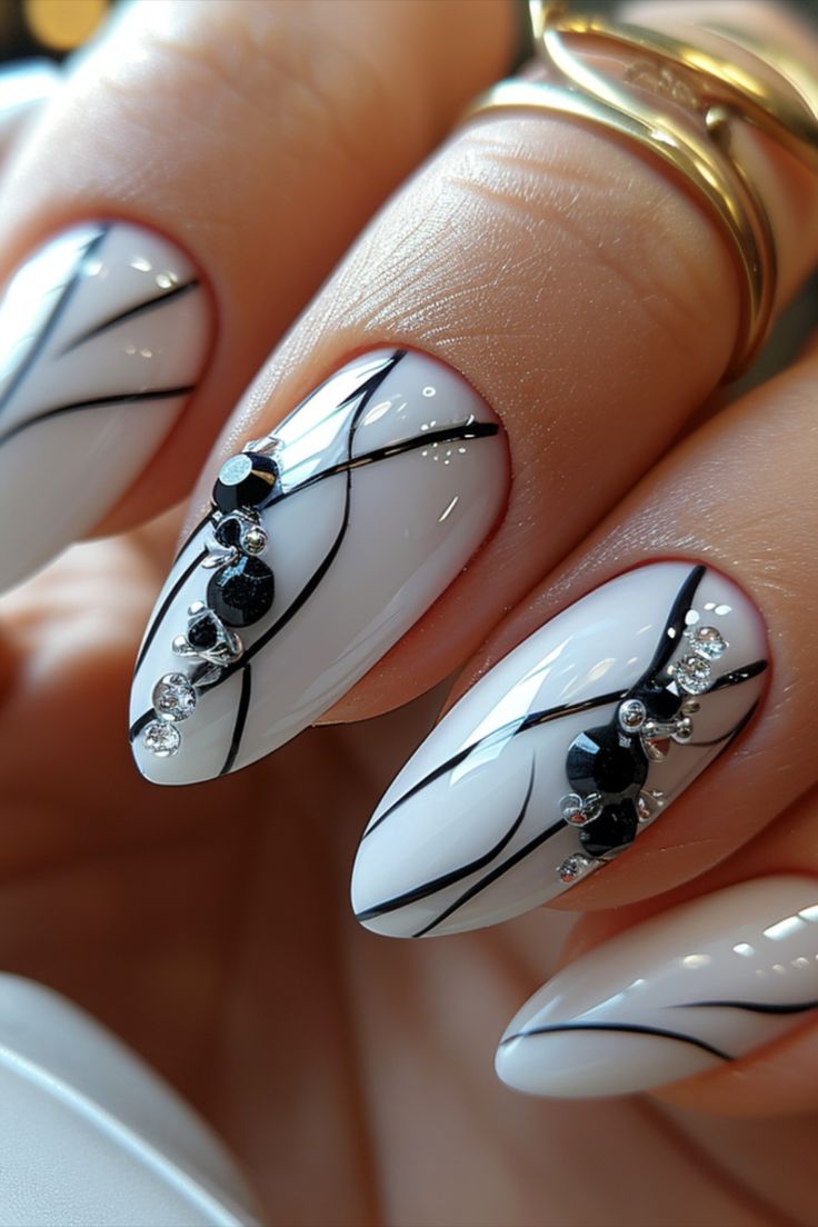 Sophisticated Glossy White Nail Design with Intricate Black Lines and Sparkling Rhinestones.