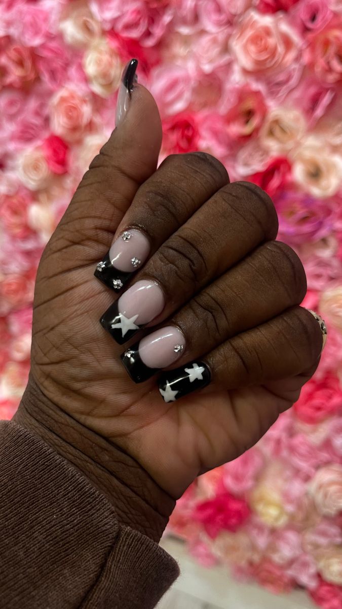 Elegant Nude and Black Nail Design with Star Motifs and Rhinestones.