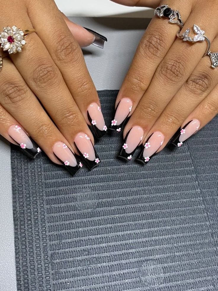 Chic Nail Design: Soft Pink and Bold Black Tips with Floral Accents.