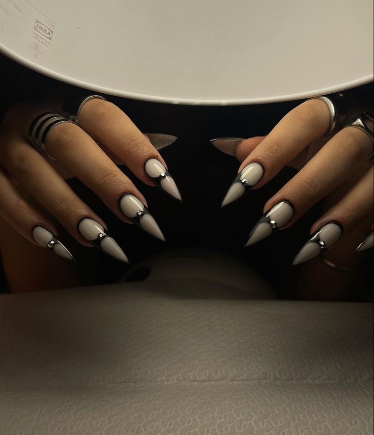 Striking Stiletto Nails: Glossy White Base with Sharp Black Tips and Glamorous Metallic Accents.