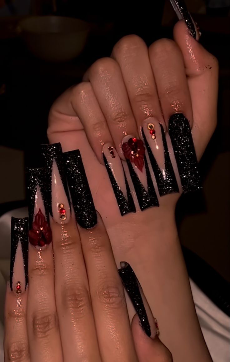 Striking Black and Nude Angular Nail Design with Elegant Floral Details and Red Gem Accents.