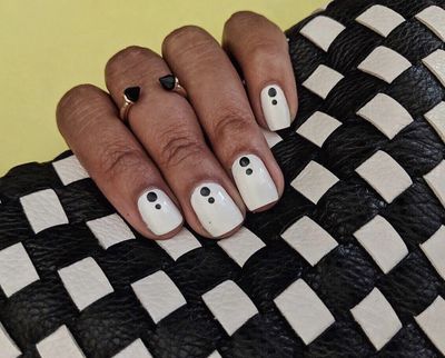 Chic Glossy White Nails with Minimalistic Black Dots and Textured Clutch Accents.