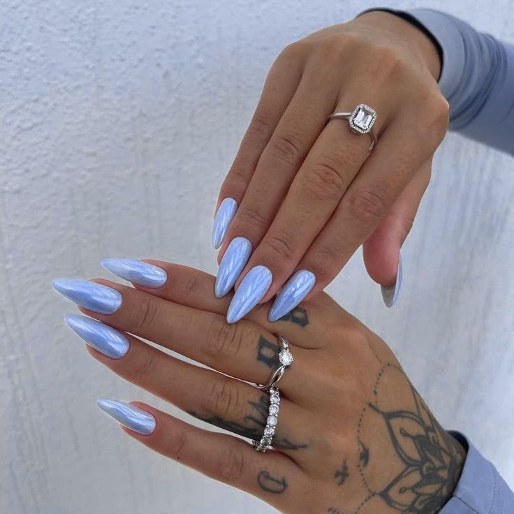 Chic Elegant Pastel Blue Almond Nails Enhanced with Intricate Tattoos and Stylish Rings.