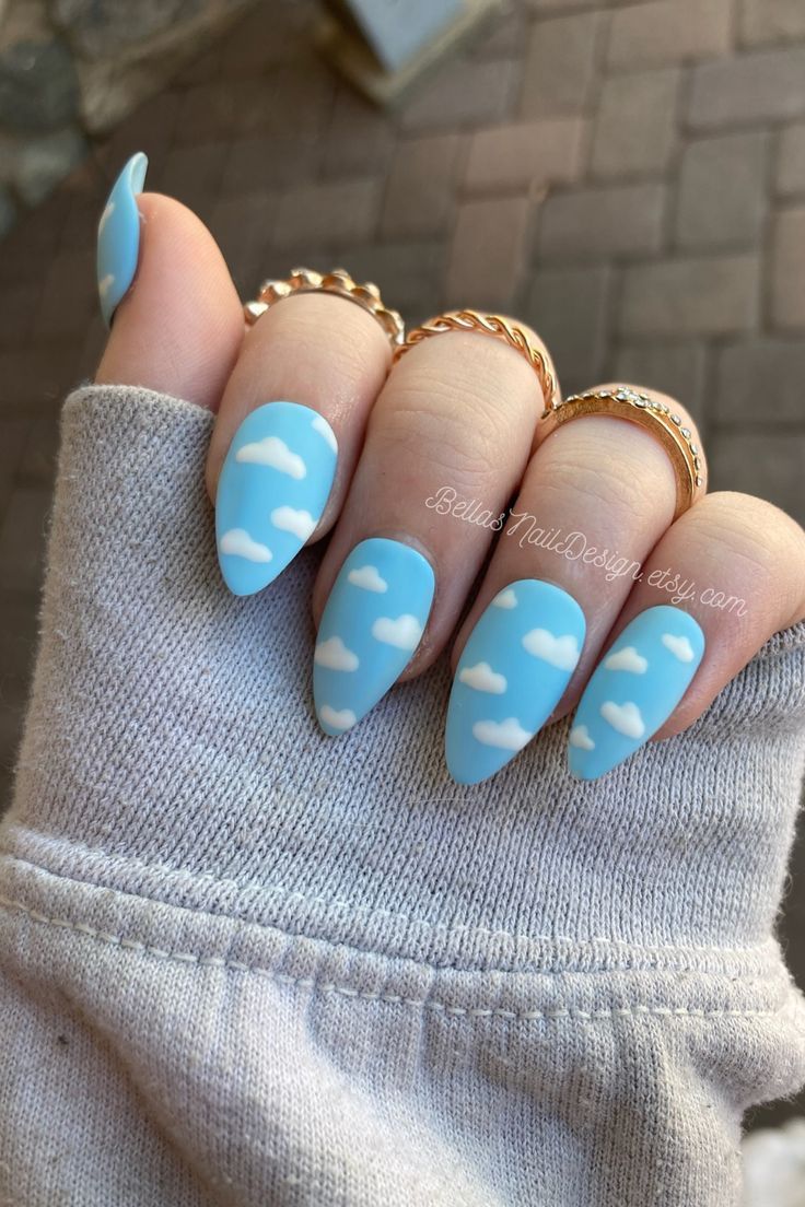 Whimsical Cloud-Themed Nail Design with Elegant Almond Shape and Trendy Gold Accents.