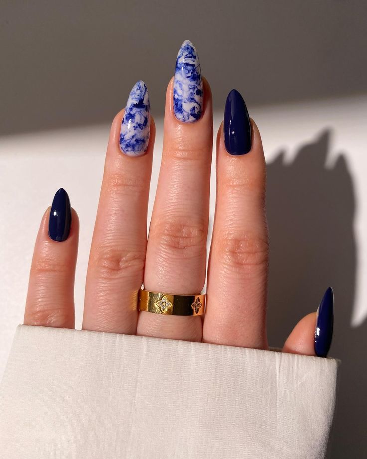 Chic Deep Navy and Marbled Blue Nail Design with Elegant Tapered Shape and Gold Ring Accents.