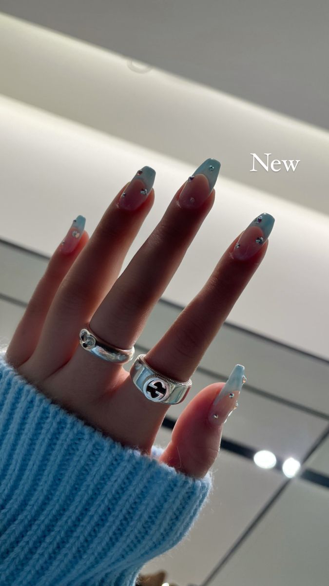 Chic Light Blue and White Nail Design Adorned with Gems and Styled with Rings.