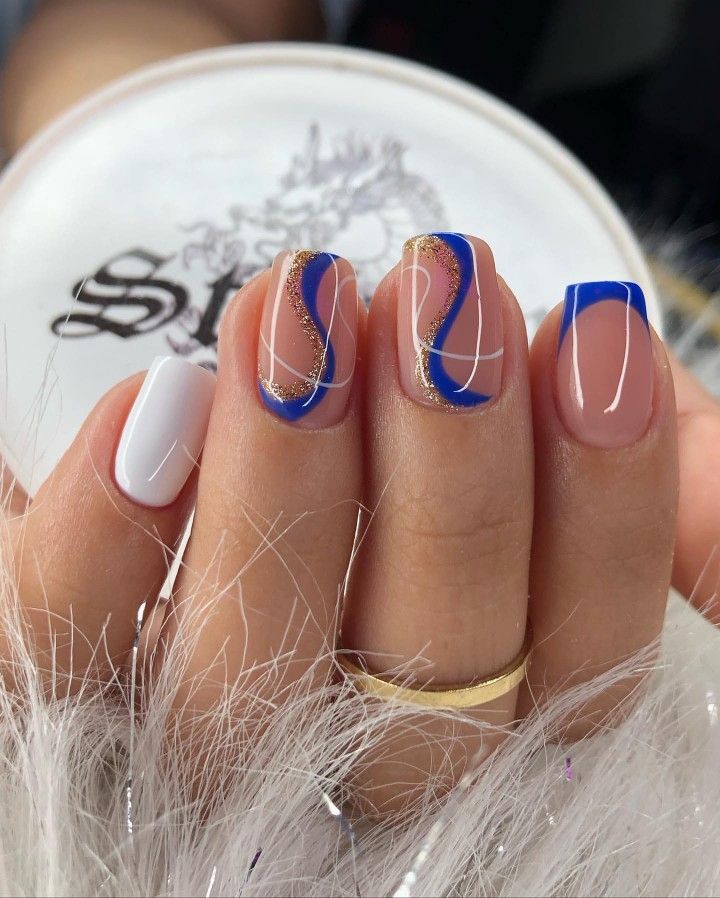 Chic Nail Design: Elegant Nude and Bold Blue with Gold Accents and Minimalist White Accent.