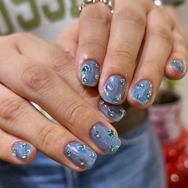 Dreamy Lavender Nail Design with Shimmering Glitter and Colorful Gemstones for Playful Elegance.