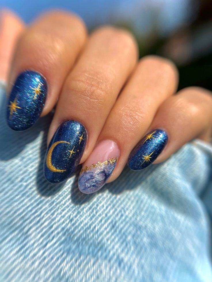 Celestial Nail Design: Deep Blue Base with Glittery Moons, Stars, and Ethereal Marble Accent.