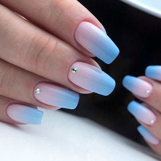 Elegant Ombre Nail Design: Soft Blue to Pastel Pink Gradient with Rhinestone Sparkles on Square-shaped Nails.