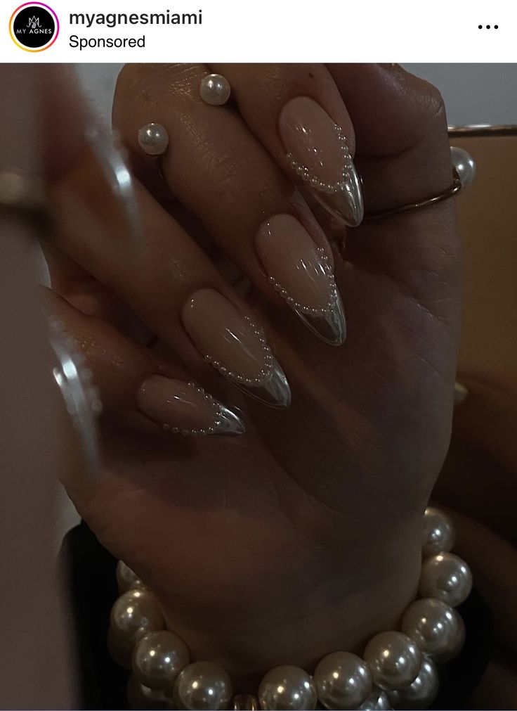 Chic Stiletto Nail Design in Nude and Metallic Tones with Pearl Accents and Bracelet.