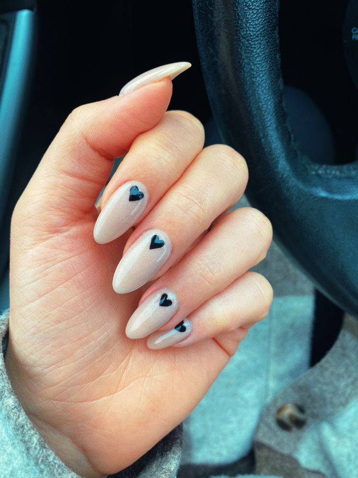 Chic Almond-Shaped Nails with Playful Black Heart Designs on Soft Nude Base.