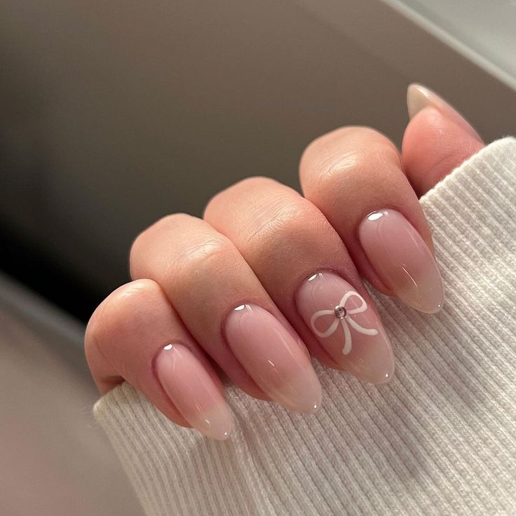 Chic Ombre Nail Design: Nude to Sheer Pink with Playful White Bow Accents.