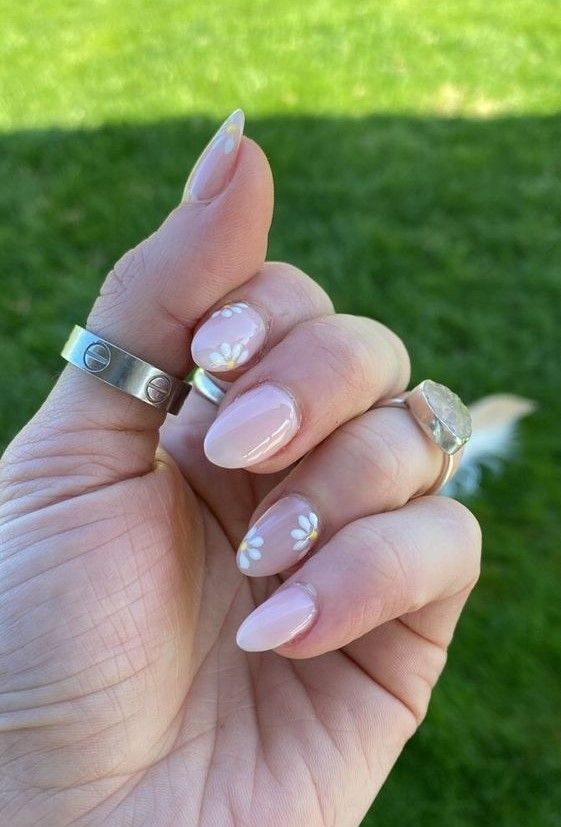 Elegant Almond-Shaped Nude Nails with White Floral Accents and Silver Rings for Any Occasion.