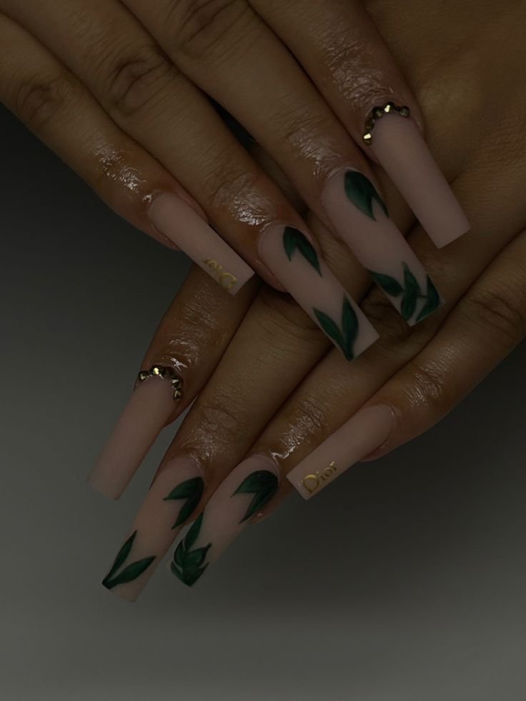 Sophisticated Nude Nail Design with Dark Green Leaf Motifs and Glamorous Metallic Accents.