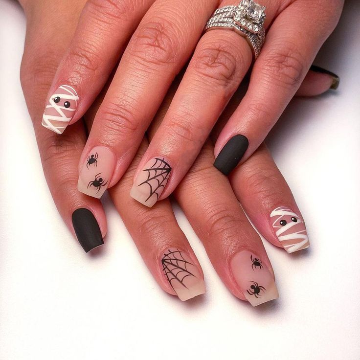 Halloween Nail Art: Spooky Matte Black & Nude Design with Spiderwebs and Mummy Motifs.