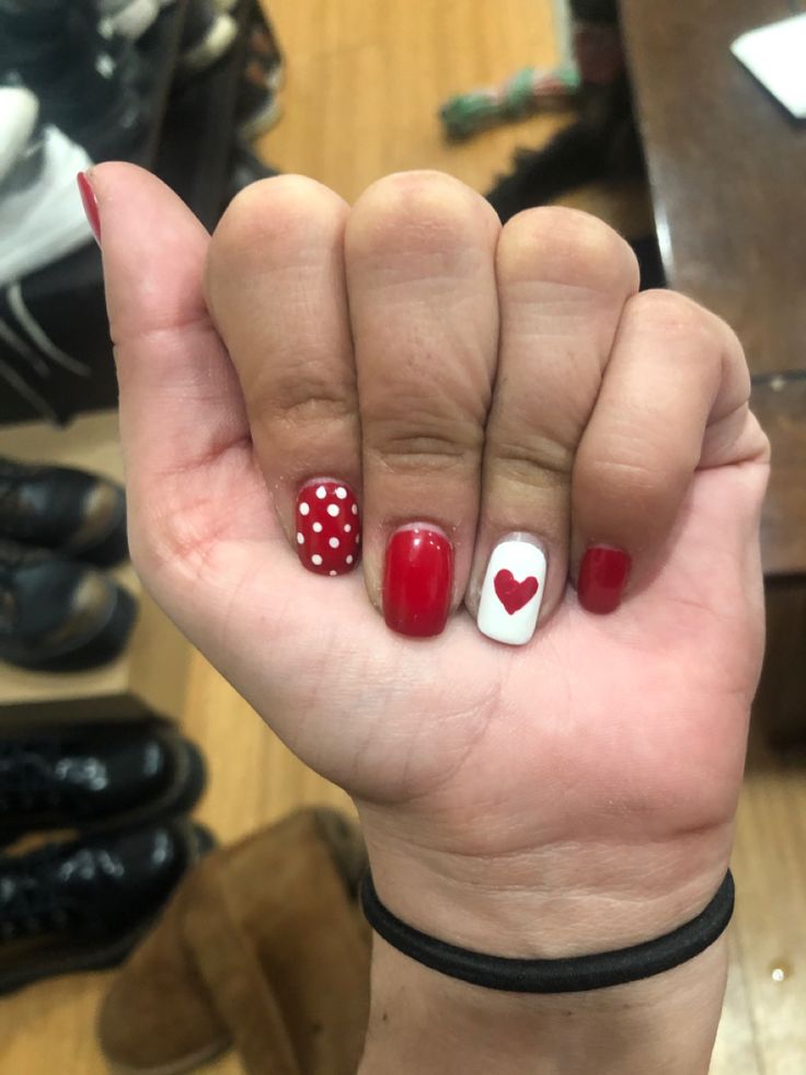 Playful Nail Design: Vibrant Red Base with Charming Polka Dots and Romantic Heart Accent.