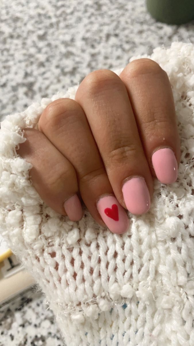 Chic Soft Pink Nail Design with Playful Red Heart Accent for Romantic Occasions.