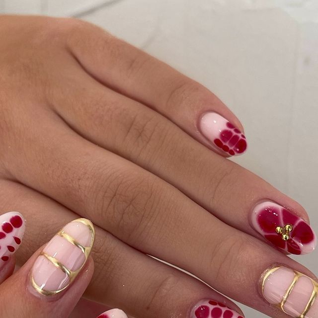 Chic Nail Design: Soft Pink and Bold Red with Geometric Gold Accents and Floral Patterns.