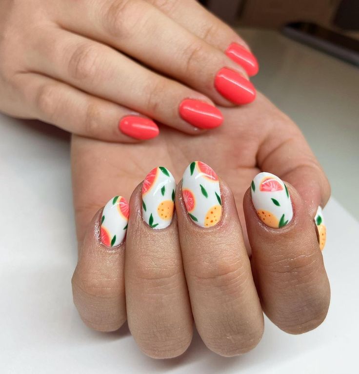 Vibrant Summer Nail Design: Colorful Fruit Motif Accented by Sleek Coral Polish.