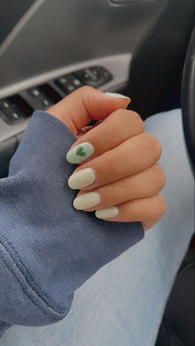 Chic Almond-Shaped Nail Design with Soft White and Playful Green Heart Accent.