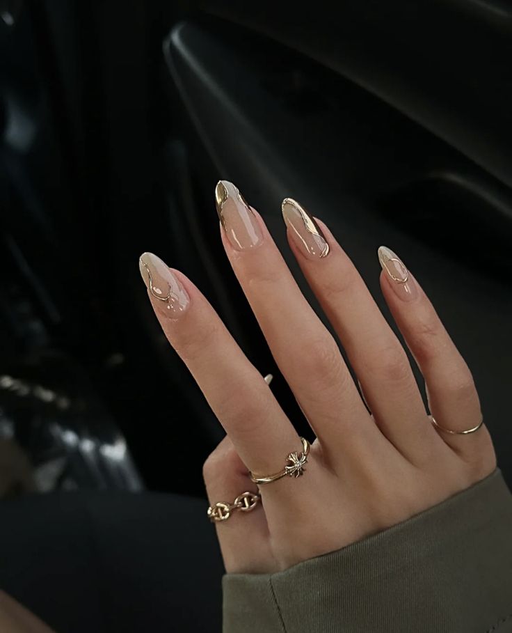 Sophisticated Almond-Shaped Nail Design: Nude Base with Gold Accents and Delicate Rings.