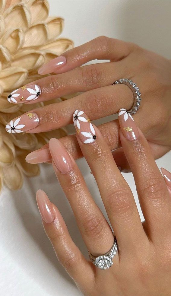 Chic Floral Nail Design: White Daisies on Nude with Black Accents and Gold Glamour.