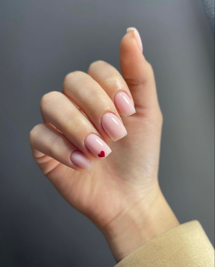 Elegant Nude Nail Design with Playful Red Heart Accent for Modern Romance.