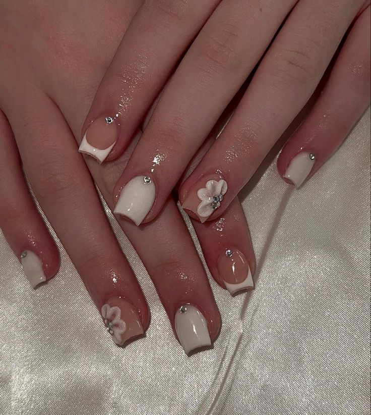 Elegant White and Nude Nail Design with Floral Accents and Sparkling Rhinestones