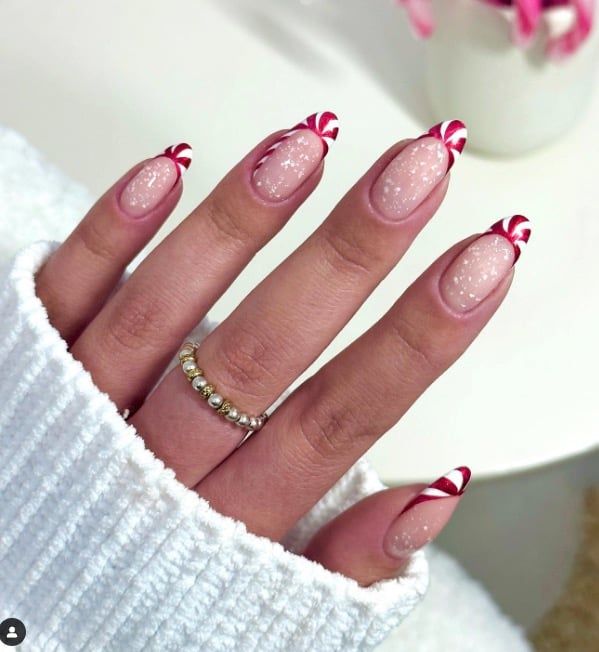 Chic Holiday Nail Design: Delicate Pink Base with Candy-Inspired Red and White Striped Tips.